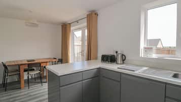 A modern kitchen with grey cabinets, a wooden dining table, and a window with a view of a house.