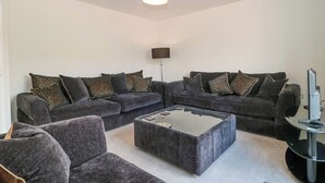 A modern living room with a sectional sofa, a glass coffee table, and a floor lamp. - Beacon View (Malvern)
