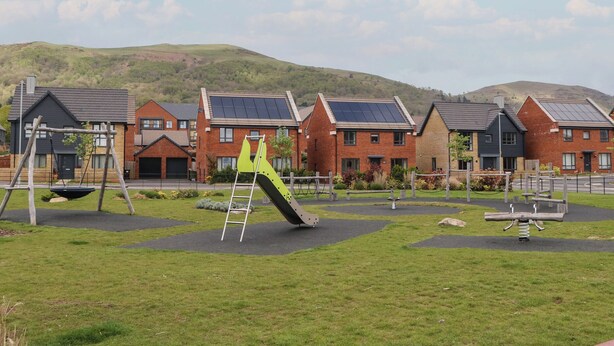 A playground with swings and a slide, surrounded by houses with solar panels. - Beacon View (Malvern)