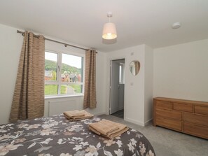 Ein Schlafzimmer mit Bett, Schminktisch, einem Fenster mit Vorhängen, einer Heizung und Blick auf Häuser.