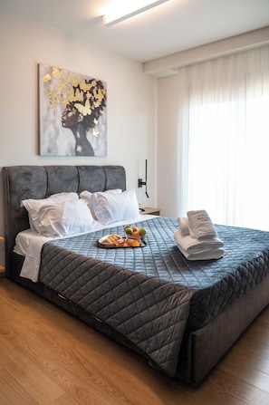 Un dormitorio con cama, almohadas, colcha, mesita de noche con lámpara y un cuadro en la pared.