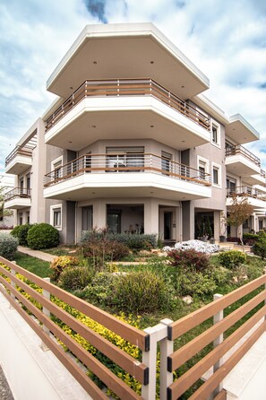 Um edifício residencial com várias andares, varandas, um jardim ajardinado e um banco de madeira.