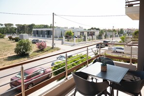 Un balcón con mesa y sillas, vista a una calle con coches y un edificio de diseño moderno.