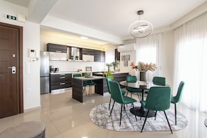 Una cocina moderna con armarios oscuros, una isla central y una zona de comedor con sillas verdes.