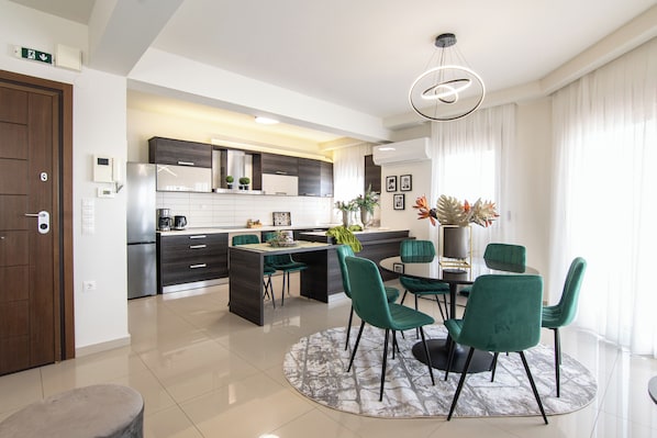 A modern kitchen with dark cabinetry, a central island, and a dining area with green chairs.