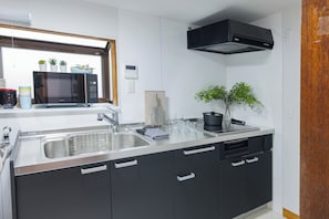 A modern kitchen with a stainless steel sink, black cabinets, a microwave, and a window with potted plants. - RYO  (Sajima, Yokosuka)