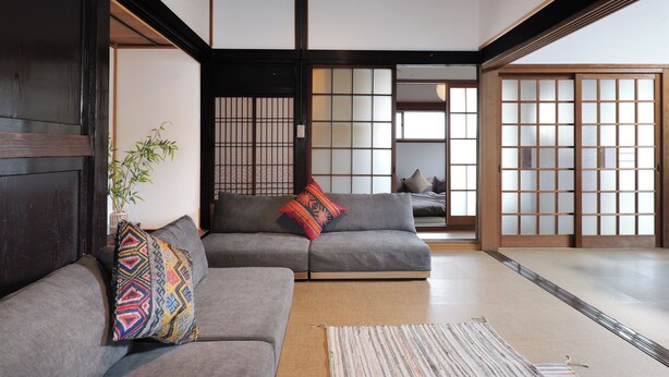 A traditional Japanese interior with tatami flooring, a grey sofa with patterned cushions, and sliding doors.