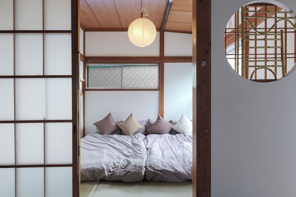 Ein traditioneller japanischer Raum mit Tatami-Bodenbelag, einer Futon-Liege, Shoji-Schiebetüren und einem runden Fenster.