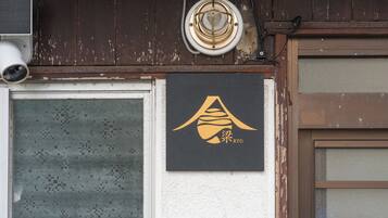 A building facade with a weathered brown wooden exterior, a security camera, and a black sign with gold lettering.