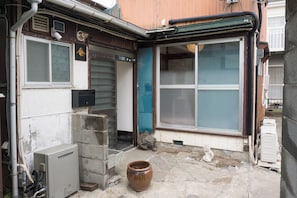 A corner of a building with a large window, a small utility box, and a stone wall.
