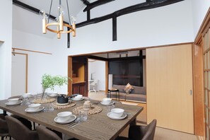 A dining area with a wooden table set for four, surrounded by chairs, with a hanging light fixture above. - RYO  (Sajima, Yokosuka)