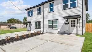 A two-story residential building with a front porch, a garage, and a well-maintained lawn. - Reed Unit B - Quiet Solo Room w/Shared Bath in Co-Living Home (Houston)