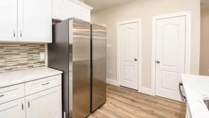 A modern kitchen with white cabinets, a stainless steel refrigerator, wooden flooring, and white doors. - Reed Unit B - Quiet Solo Room w/Shared Bath in Co-Living Home (Houston)