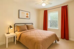 A bedroom with a bed, a nightstand, a lamp, a ceiling fan, and a window with curtains. - Reed Unit B - Entire Spacious 4BR Home (Houston)