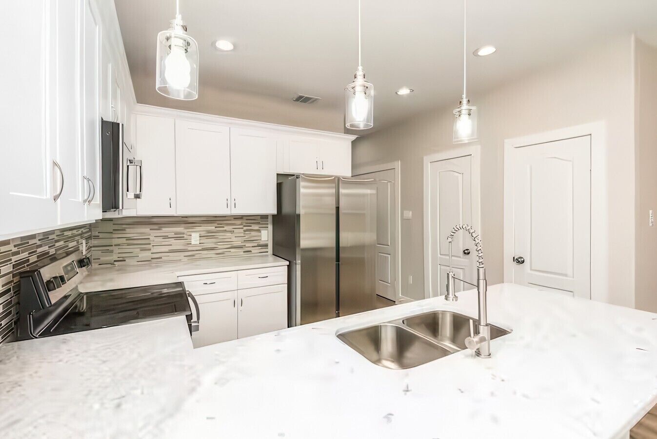 Une cuisine moderne avec des meubles blancs, un réfrigérateur en acier inoxydable, un plan de travail en marbre et des luminaires suspendus.