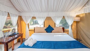 A tented room with a bed, a table with a tray, and a view of the outdoors. - Farm Aravalia (Faridabad)