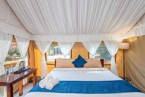 A tented room with a bed, a table with a tray, and a view of the outdoors. - Farm Aravalia (Faridabad)