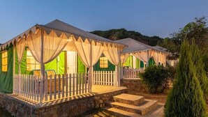 A row of tents with a white picket fence, steps leading to the entrance, and a stone base. - Farm Aravalia (Faridabad)