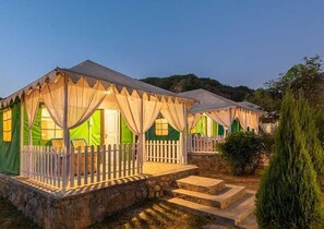 A row of tents with a white picket fence, steps leading to the entrance, and a stone base. - Farm Aravalia (Faridabad)