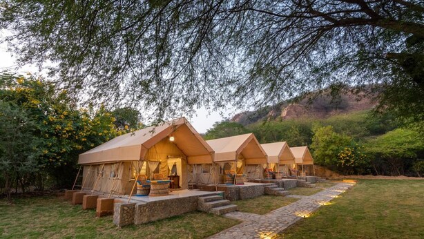 A row of tents with stone steps leading to the entrance, surrounded by greenery and a stone pathway. - Farm Aravalia (Faridabad)
