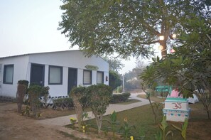 A building with a reception area, a pathway leading to it, and a sign with a symbol. - Farm Aravalia (Faridabad)