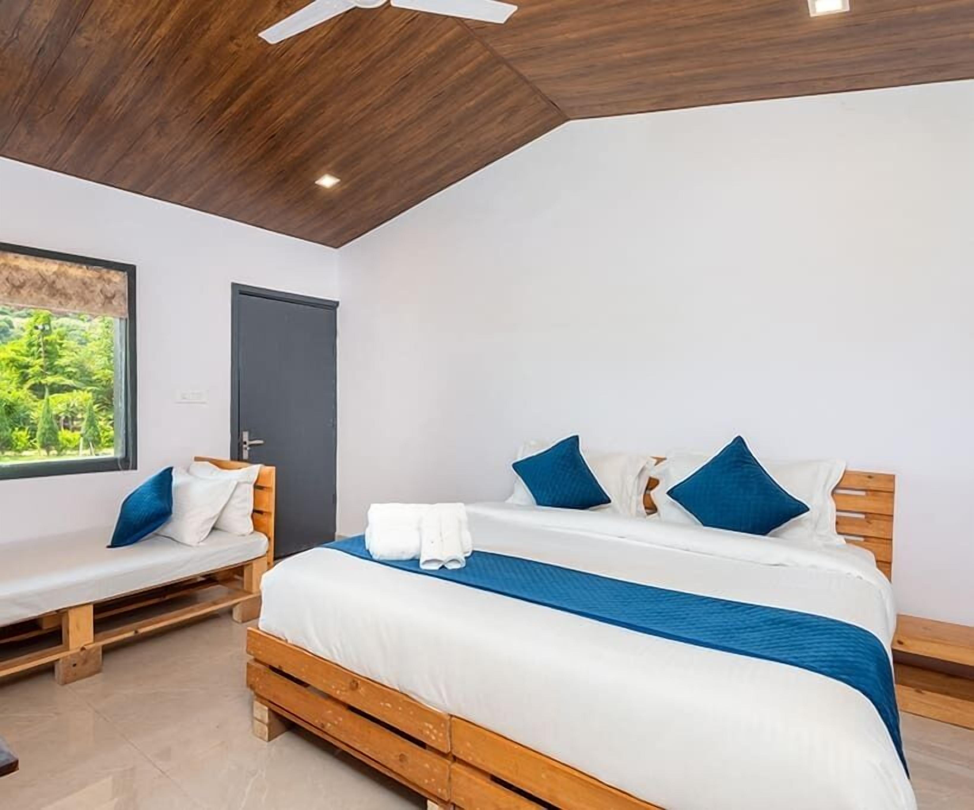 A bedroom with a wooden bed, a bench, and a window with a view of greenery.