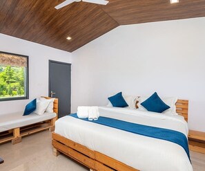 A bedroom with a wooden bed, a bench, and a window with a view of greenery. - Farm Aravalia (Faridabad)