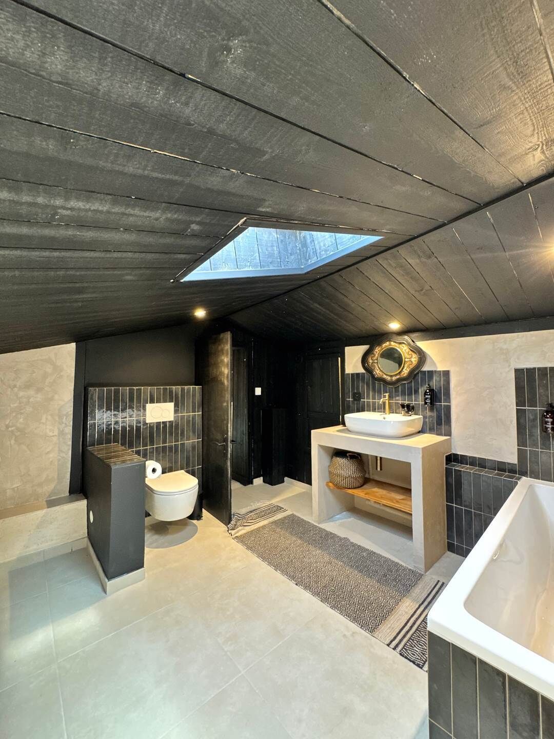 Un baño moderno con tragaluz, bañera, inodoro y tocador con espejo.