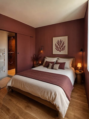 A bedroom with a large bed, a wooden floor, a door leading to a bathroom, and a wall-mounted artwork. - Dulse Room with Private Bathroom (LE BOIS PLAGE EN RE)