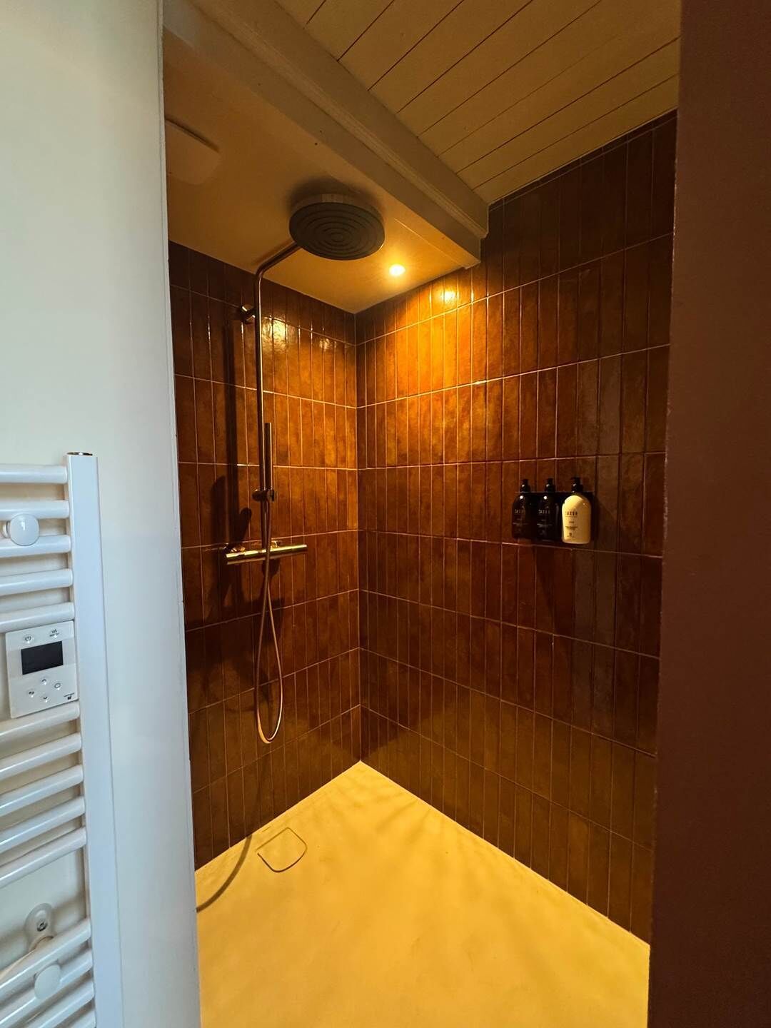 Una ducha con panel de control, cabezal de ducha manual y una alfombra de baño amarilla.