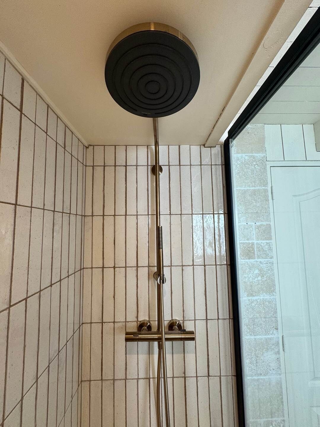 Une douche dotée d’un pommeau circulaire, d’une barre verticale et d’une barre horizontale.