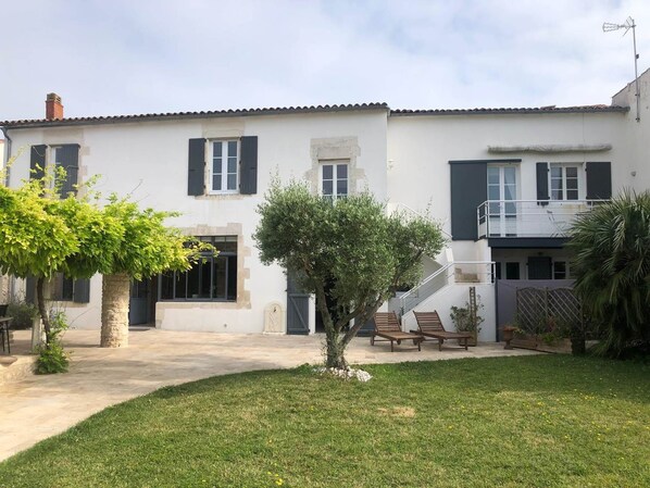 A two-story house with a white facade, black shutters, and a small garden with a tree and a bench. - Fleur de Sel Room with Private Bathroom (LE BOIS PLAGE EN RE)