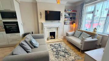 Ein Wohnzimmer mit Kamin, Sofa, Fernseher und Bücherregal.