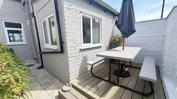 A patio area with a table and chairs, a small garden, and a white brick building.