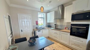 A modern kitchen with white cabinets, a built-in oven, and a window. - The Hideaway - A Cosy Beachside Retreat (Fleetwood)