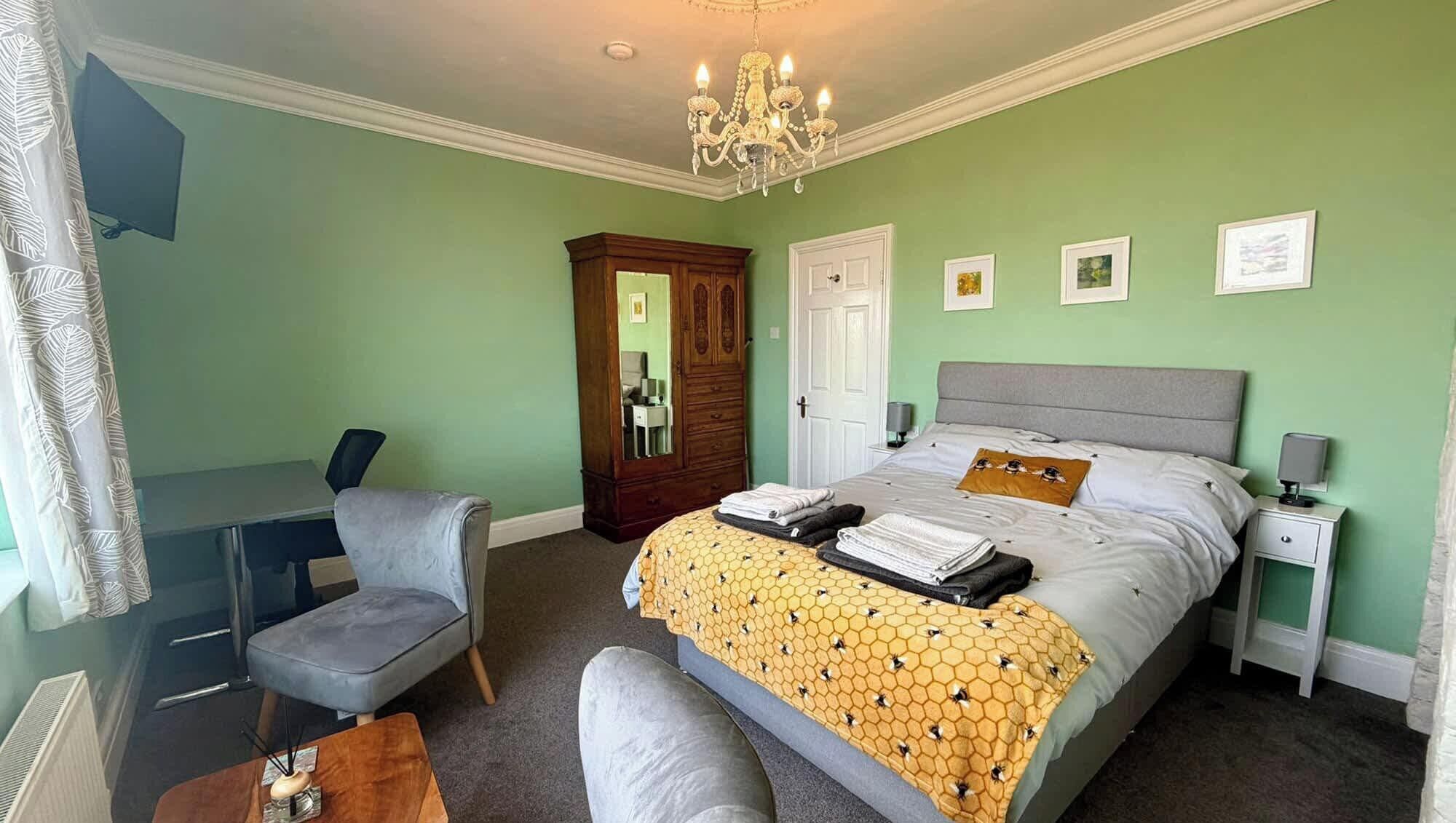 Une chambre à coucher comprenant un lit, un bureau, une chaise, une commode et un lustre.