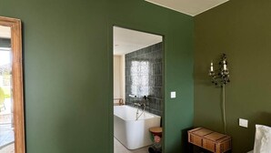 A bedroom with a green wall, a bed with white bedding, a bedside table, a lamp, and a view into the bathroom. - Criste Marine Deluxe Suite (LE BOIS PLAGE EN RE)