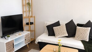Ein modernes Wohnzimmer mit einem Flachbildfernseher, einem Holz-TV-Schrank, einem Sofa mit gemusterten Kissen, einem Couchtisch mit Kerzen und einem Teppich mit Fischgrätmuster.