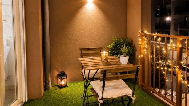 Eine kleine Terrasse mit einem Holztisch und -stühlen, einem Blumentopf und Lichterketten.