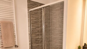 Ein modernes Badezimmer mit Duschkabine aus Glas, einem Holzwaschtisch, einer schwarzen Badmatte und einem Blumentopf.