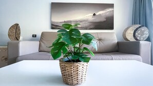 Ein Wohnzimmer mit einer Couch, einem Couchtisch, einer Topfpflanze und einem an der Wand hängenden Kunstwerk, das einen Surfer zeigt.
