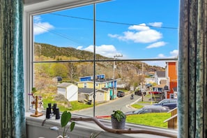 A window view of a residential street with houses, a clear sky, and a power line.