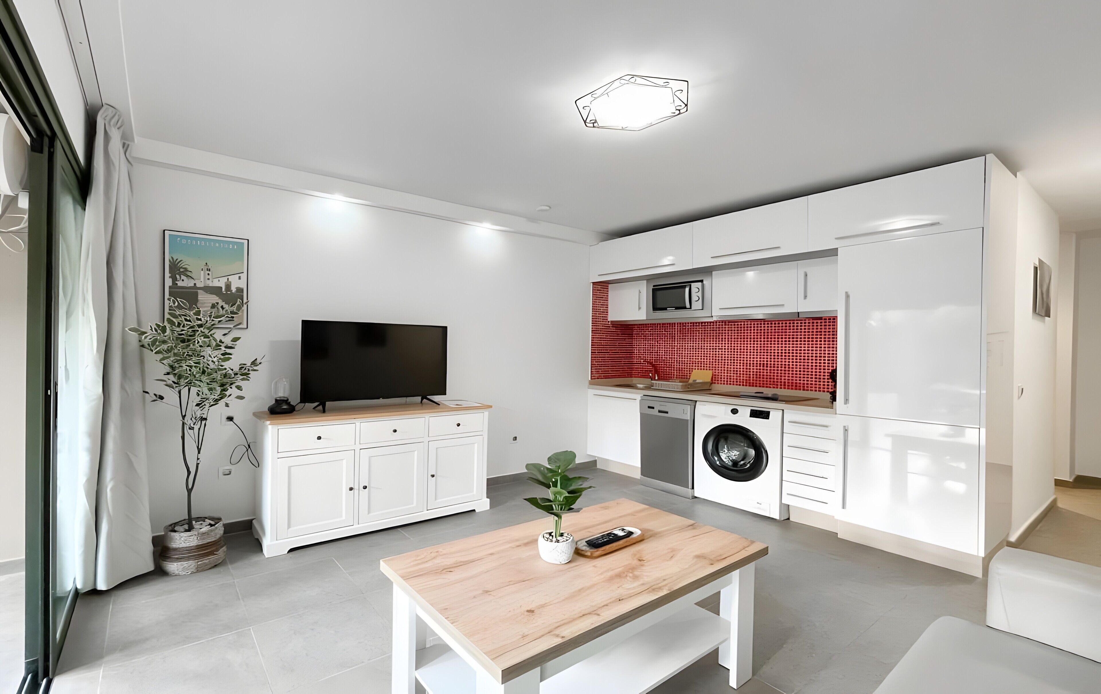 Una cocina moderna con armarios blancos, un salpicadero rojo, una lavadora y un televisor de pantalla plana.