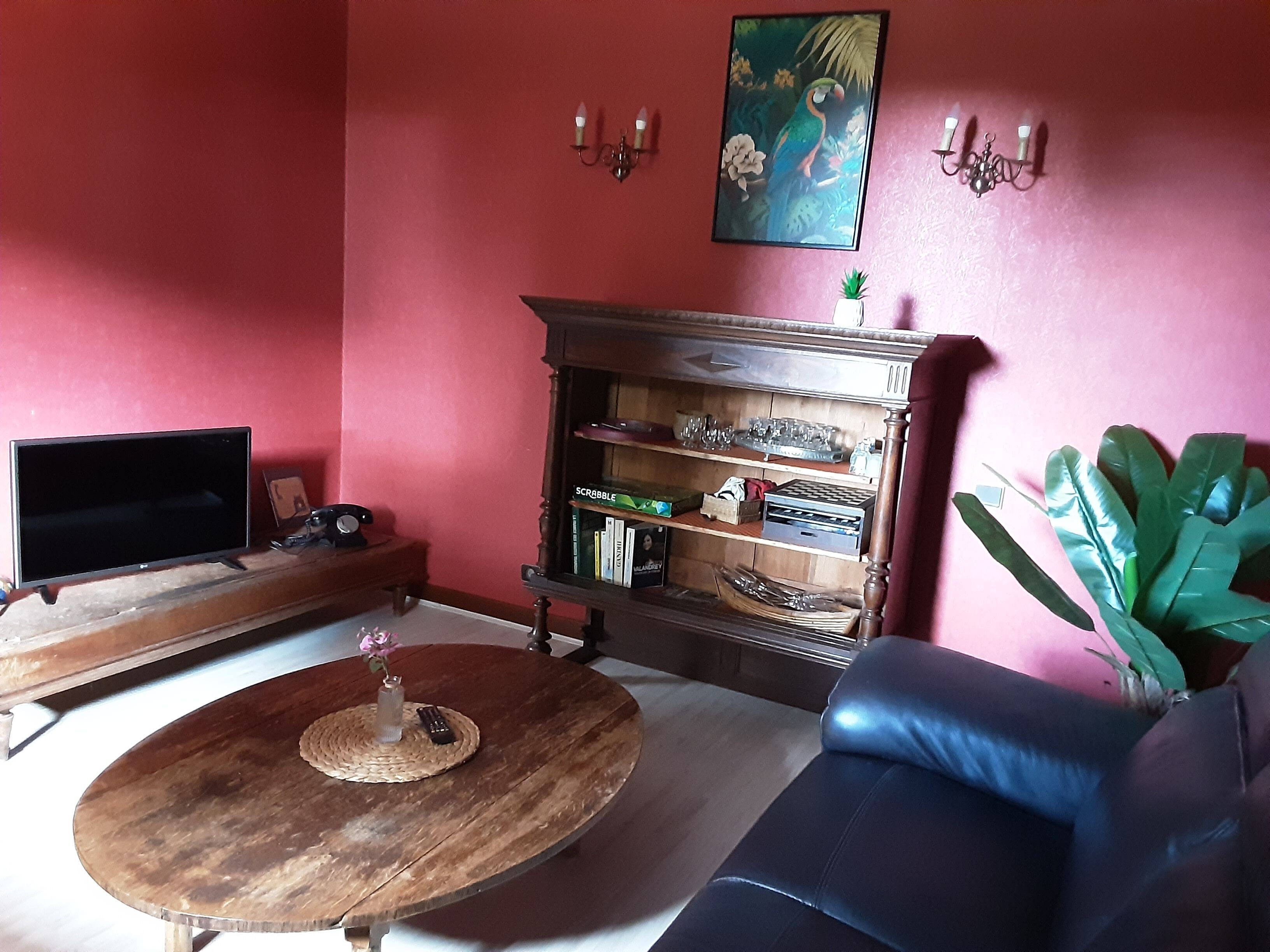 A living room with a TV, a wooden coffee table, a bookshelf, a sofa, and a potted plant.