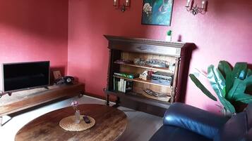 A living room with a TV, a wooden coffee table, a bookshelf, a sofa, and a potted plant.