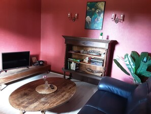 A living room with a TV, a wooden coffee table, a bookshelf, a sofa, and a potted plant. - Maison de caractère .La vague douce des Landes (Vielle-Saint-Girons)
