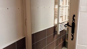Un pasillo estrecho con suelo de baldosas, una puerta blanca con manija negra y un radiador blanco en la pared.