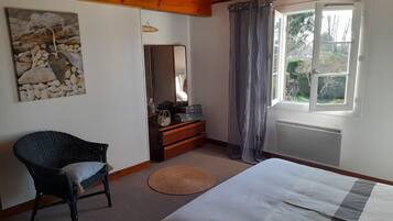 A bedroom with a bed, a chair, a dresser, a mirror, a window with curtains, and a wall-mounted picture.