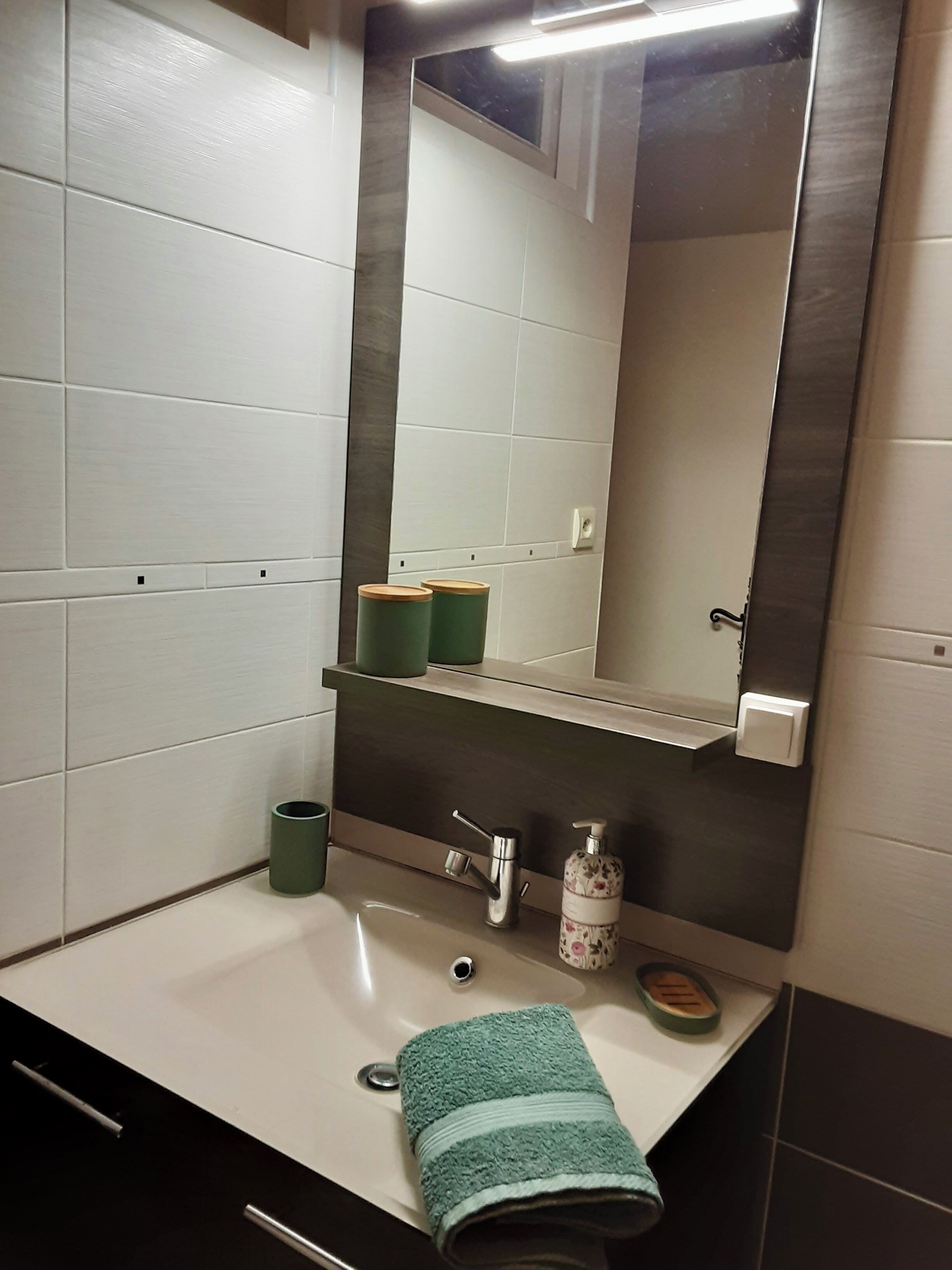 Une salle de bain avec un miroir, un lavabo et deux récipients verts placés sur une étagère.