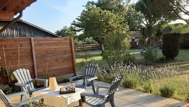 Un patio al aire libre con una mesa y sillas, rodeado por una cerca de madera y diversas plantas.